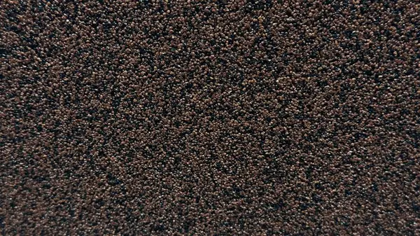 Koyu tanecikli bir yüzeye yakın çekim, yoğun bir şekilde paketlenmiş küçük kahverengi ve siyah tanecikler, teknik bir karakterle tek bir doku oluşturur..
