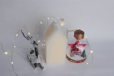 Metalik Ren Geyiği, Ev Şeklinde Mum ve Beyaz Arkaplan Üzerine Noel Baba Festivali Kompozisyonu ile Kar Küresi 'nin yer aldığı Noel Süslemeleri