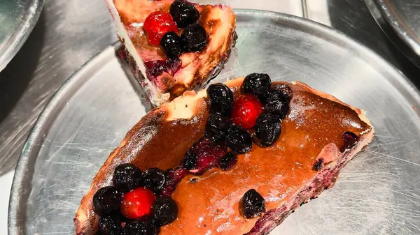 Metal tabakta yabanmersini ve kirazlı iki dilim ev yapımı cheesecake pişmiş ürünlerin, menülerin, mutfak bloglarının ve mevsimsel içeriklerin reklamları için iştah açıcı bir tatlı..