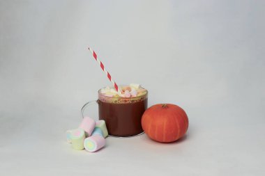 Beyaz arka planda renkli marşmelovlar ve turuncu balkabaklı kakao. Reklam içecekleri, yemek içeriği, sosyal medya tasarımı, kartpostallar, kafe menüleri için samimi bir sonbahar kompozisyonu.