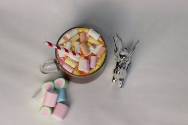 Renkli marşmelovlu sıcak kakao fincanı ve süslü çizgili kamışın yanında, kış reklamları için mükemmel bir tatil fotoğrafı, Noel kartları, kahve menüleri ve rahat yaşam tarzı içeriği.