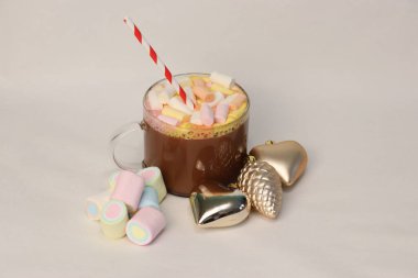 Kışın reklam kampanyaları, kafe menüleri, Noel tebrik kartları ve sosyal medya içeriği için kalp ve çam kozalağı şenliği fotoğrafı şeklinde altın Noel süslerinin yanında kırmızı ve beyaz pipetli sıcak kakao.