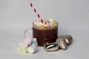 Kışın reklam kampanyaları, kafe menüleri, Noel tebrik kartları ve sosyal medya içeriği için kalp ve çam kozalağı şenliği fotoğrafı şeklinde altın Noel süslerinin yanında kırmızı ve beyaz pipetli sıcak kakao.