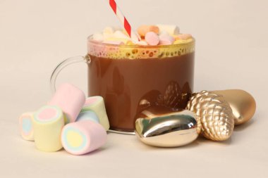 Kışın reklam kampanyaları, kafe menüleri, Noel tebrik kartları ve sosyal medya içeriği için kalp ve çam kozalağı şenliği fotoğrafı şeklinde altın Noel süslerinin yanında kırmızı ve beyaz pipetli sıcak kakao.