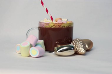 Kışın reklam kampanyaları, kafe menüleri, Noel tebrik kartları ve sosyal medya içeriği için kalp ve çam kozalağı şenliği fotoğrafı şeklinde altın Noel süslerinin yanında kırmızı ve beyaz pipetli sıcak kakao.