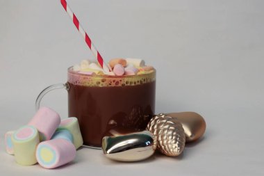 Kışın reklam kampanyaları, kafe menüleri, Noel tebrik kartları ve sosyal medya içeriği için kalp ve çam kozalağı şenliği fotoğrafı şeklinde altın Noel süslerinin yanında kırmızı ve beyaz pipetli sıcak kakao.