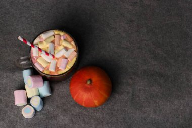 Gri arka planda balkabağının yanına çizgili kamış ve kremalı sıcak kakao.