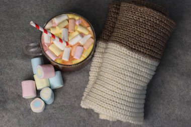 Marşmelovlu lezzetli sıcak kakao ve gri arka planda örülmüş ekosenin yanında kırmızı-beyaz kamış mevsimlik reklamlar için sıcak ve samimi fotoğraf, kafe menüleri, sosyal medya, tebrik kartları ve sonbahar-kış içeriği.