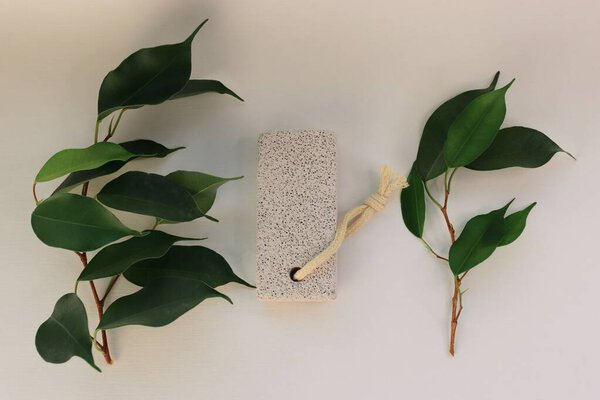 Пумитический камень для ухода за ногами на белом фоне с зелеными листьями натуральный инструмент для педикюра, удаление мозолей и спа-процедур
