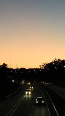 Şehir yaşamı, seyahat, taşınabilirlik, ulaşım altyapısı, araba reklamcılığı veya web siteleri ve sunumlar için arka plan konuları için günbatımı manzaralı gökyüzü altında arabaları ve sokak lambaları olan akşam otoyolu ideal görüntü