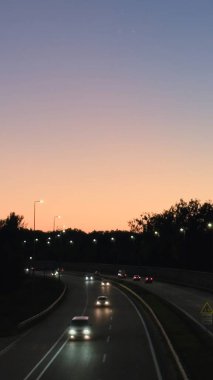 Şehir yaşamı, seyahat, taşınabilirlik, ulaşım altyapısı, araba reklamcılığı veya web siteleri ve sunumlar için arka plan konuları için günbatımı manzaralı gökyüzü altında arabaları ve sokak lambaları olan akşam otoyolu ideal görüntü