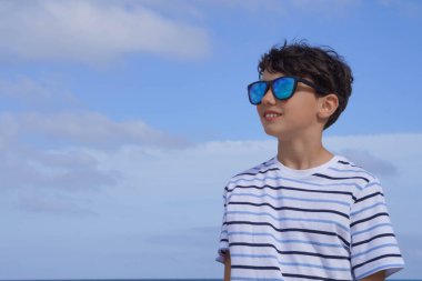 Güneş gözlüklü ve mavi gökyüzü ufka bakan bir genç.