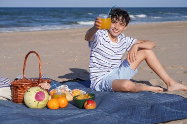 Gençlik öncesi plajda piknik yapar, bir bardak portakal suyuyla mutlu bir şekilde kadeh kaldırır.