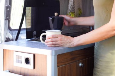 Kadın bir karavanın mutfağında kahve hazırlıyor.