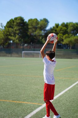 Genç bir çocuk futbol oynuyor ve içeri giriyor.