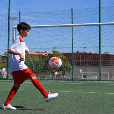 futbol sahasında futbol antrenmanına odaklanan genç bir çocuk. Arka planda ekipman ve gol var.