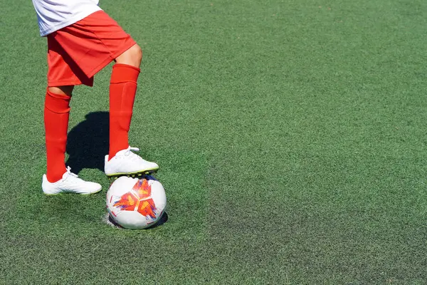 Penaltı atmadan önce futbol topuna basan bir çocuğun bacakları ve ayakları.