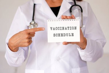 Kadın doktor işaret parmağıyla aşı programına işaret ediyor.
