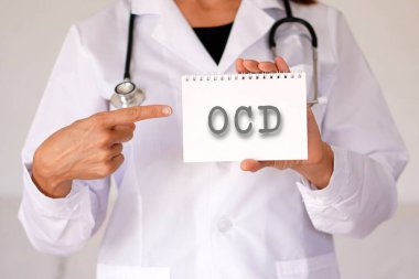 Kadın doktor parmağıyla bir deftere işaret ediyor. OKB kısaltması.