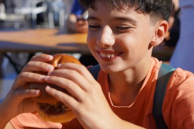Sokak yemeği. Mutlu çocuk, ısırmadan önce bir hamburgere bakıyor.