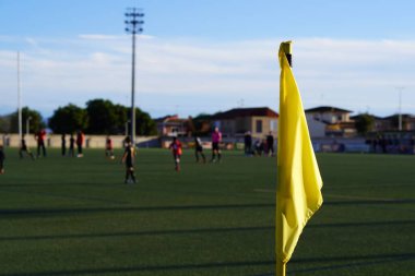 Bir çocuk futbol maçında futbol sahasında sarı köşe bayrağı. Oyuncular ve hakem arka planda..