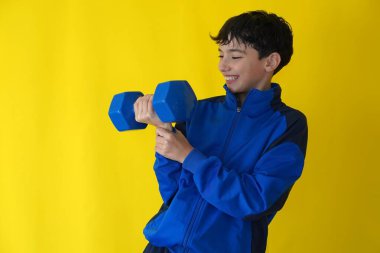 Sağlıklı yaşam. Dambıl egzersizi yapan genç bir çocuk. Mavi spor giyim ve sarı arkaplanlı.