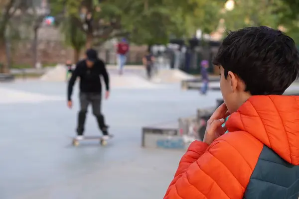 Çocuk, paten kaymayı öğrenmeden önce kaykaycıları ilgiyle izliyor.