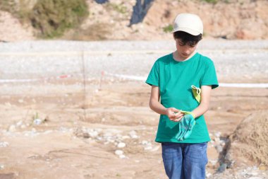 Kurak bir bölgeyi temizlemek ve yeniden ağaçlandırmak için iş eldiveni giyen genç bir çocuk.