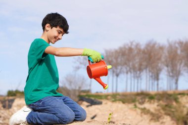 Çevresel iyileşme sırasında küçük bir bitkiyi sulayan mutlu bir gönüllü çocuk.