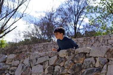 Çocuklar tatilde dışarıda doğa aktiviteleri yapıyor, taş duvarlar arasından dışarı bakıyor.