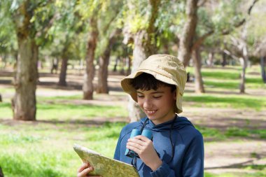 Genç bir çocuk tatilde ya da elinde dürbün ve pusula ile geziyor.