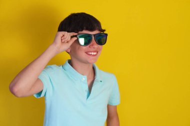 seyahat ve tatil. Sarı arka planda güneş gözlüklü, gülümseyen çocuk..