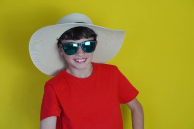 seyahat ve tatil. Sarı arka planda plaj şapkalı ve güneş gözlüklü çocuk gülümsüyor..