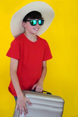 seyahat ve tatil. Bavullu, güneş gözlüklü ve sarı arkaplan şapkalı çocuk..
