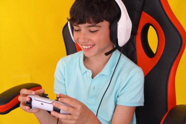 Çocuklar ve video oyunları. Genç çocuk, mikrofonlu bir kulaklıkla oyuncu koltuğunda.
