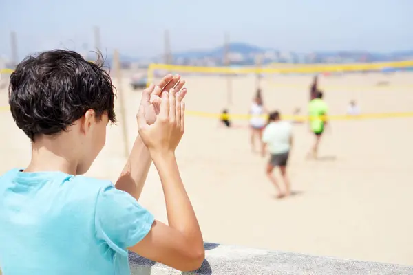 Genç çocuk yazın plaj voleybolu maçı izliyor.
