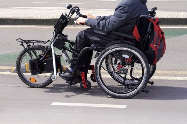 Güneşli bir günde, tekerlekli sandalyede ön tekerli sandalyede yürüyen birinin yüzsüz görüntüsü.