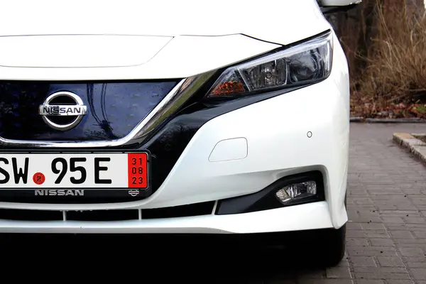 Vinnytsia, Ukrayna; 21 Şubat 2024. Beyaz Nissan Leaf farları. Elektrikli araba Nissan Leaf radyatör ızgarası. Arabanın önüne Nissan Leaf. Nissan Yaprak logosu ve amblemi. 