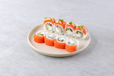 Suşi, salatalık, Philadelphia peyniri ve somonla birlikte ahşap bir arka planda siyah tahta üzerinde yuvarlanır. Japon mutfağı. Kapat.