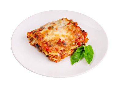 Beyaz bir tabakta servis edilen fesleğen yapraklarıyla kaplı kıymalı bolonez soslu geleneksel lazanyaya yakın çekim.,