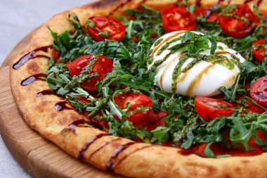 Üzerine kremalı burata, taze roka, vişneli domates, pesto ve balzamik yağmurla süslenmiş zanaatkar pizza..