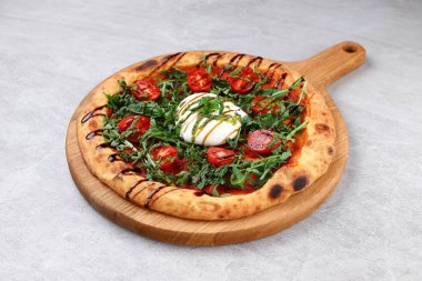 Üzerine kremalı burata, taze roka, vişneli domates, pesto ve balzamik yağmurla süslenmiş zanaatkar pizza..