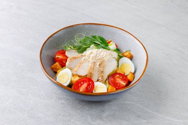 Marullu taze tavuk salatası, vişneli domates, haşlanmış yumurta, parmesan ve kıtır kıtır kızarmış ekmek gri taşlı arka planda kırsal seramik bir kasede..