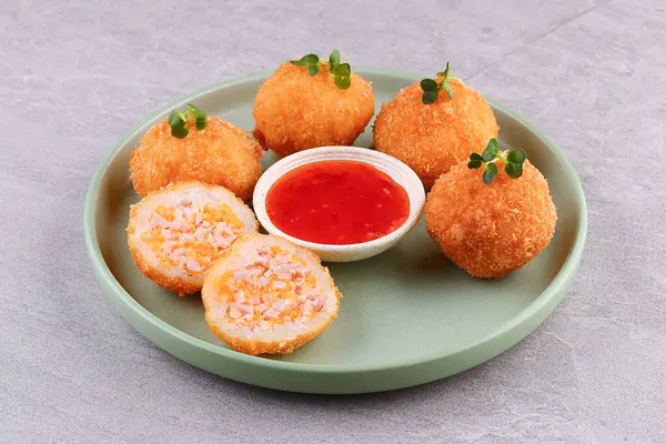 Altın pirinç peynirli kroketler, tatlı biber sosu ve taştan arka planda mikro yeşiller.