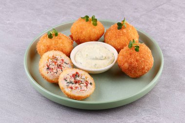 Ton balığı ve sebzelerle dolu altın pirinç kroketleri, yeşil seramik tabakta kremalı mayonez sosu ve mikro yeşillikler ile servis ediliyor..
