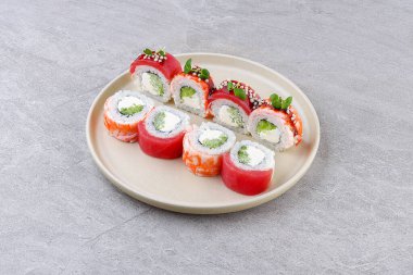 Yumuşak karides, çıtır pirinç incileri ve mikro yeşilliklerle kaplı krem peynirli ve avokadoyla dolu bir suşi rulosu, tarafsız bir arkaplanda minimalist bir tabakta servis ediliyor..