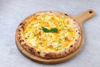 Üzerinde altın erimiş peynir, kıtır kıtır şam fıstığı ve taze fesleğen yaprağı bulunan ahşap bir kürek üzerinde taş bir arka fona servis edilen ahşap bir beyaz pizza..