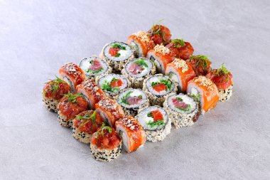 Gri taş yüzeyde sıralanmış çeşitli somon suşi rulolarının üst görüntüsü, yüksek çözünürlüklü stüdyo çekimi..