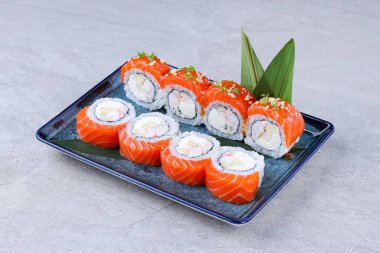 Somon suşisi, karides, krem peynir ve meyve dolgulu, mikro yeşillik ve mavi tabakta çıtır çıtır malzemeyle süslenmiş.