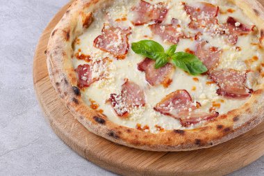 Beyaz soslu pizza üzerine çıtır pastırma rendelenmiş peynir ve taze fesleğen, ahşap bir tahtada servis edilir.